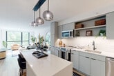 Located in Washington, DC's vibrant Shaw neighborhood, this modern one-bedroom, one-bathroom residence offers a well-designed layout across a single floor. The open-concept living and dining area is anchored by floor-to-ceiling windows that flood the space with natural light and frame lush outdoor views. Light-toned hardwood flooring runs throughout, complementing the clean, contemporary aesthetic.

The kitchen is a standout feature, equipped with stainless steel appliances including a French door refrigerator, electric range, dishwasher, and microwave. Flat-front gray cabinetry extends to the ceiling for generous storage, while white subway tile backsplash and quartz countertops add a crisp, modern finish. A central island with pendant lighting serves as both a prep space and a casual dining spot.

The bedroom is a comfortable retreat, featuring a bold floral accent wall, large floor-to-ceiling windows, and direct access to a private balcony with outdoor seating. The bathroom is finished in white tile and includes a walk-in shower and modern vanity cabinetry. Additional conveniences include an in-unit laundry area and three closets for ample storage throughout.