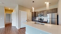 Located at 7830 Alta Dr in Columbus, Ohio, this single-floor residence offers a thoughtfully designed open-concept layout that seamlessly connects the living, dining, and kitchen areas. The living room is bright and spacious, featuring warm wood-look plank flooring, a ceiling fan, large windows with blinds that invite natural light, and direct access to an outdoor area via a glass-paneled door.

The kitchen is a standout feature, equipped with dark espresso-toned shaker-style cabinetry extending floor to ceiling, stainless steel appliances including a refrigerator, electric range, and microwave, a subway tile backsplash, and light quartz countertops. A generous kitchen island with an undermount sink and pendant lighting provides both additional prep space and a casual gathering area.

The bedroom is carpeted and features a window with blinds, providing a quiet and comfortable retreat. The bathroom is well-appointed with a dark wood vanity, white quartz countertop, a framed mirror with vanity lighting, and a shower-tub combination. Throughout the unit, neutral warm-toned walls and textured ceilings contribute to a cohesive and move-in-ready aesthetic.