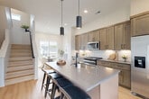 This four-story townhouse at Pecan Plaza in Elkhorn, Nebraska offers a thoughtfully designed layout across multiple levels, combining modern finishes with functional living spaces. The main living floor features an open-concept kitchen and living area anchored by a large island with bar seating, warm wood-toned cabinetry, a subway tile backsplash, stainless steel appliances, and pendant lighting — all complemented by light hardwood flooring that runs throughout. The adjacent living area provides a comfortable, airy setting with neutral tones and natural light. A separate dining area completes this social floor. The two bedrooms are generously proportioned, each filled with natural light from large windows that frame neighborhood views. The primary bedroom is notably spacious and features a walk-in closet with built-in shelving and hanging rods. Three well-appointed bathrooms with clean tile finishes serve the home. A dedicated laundry room houses full-size washer and dryer units with overhead shelving for added storage. The uppermost level offers a versatile flex space, ideal as a home office or study, with a bright window overlooking the surroundings. Stairwells are cleanly finished, maintaining the home's modern, cohesive aesthetic throughout every floor.