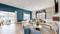 Located at 200 Villas Dr in Lavon, TX, this single-floor community amenity space is thoughtfully designed to serve as a vibrant social hub. The open-concept layout accommodates multiple activity zones, each with its own distinct character while flowing seamlessly into one another.

A bold teal accent wall anchors the recreation area, which features a ping-pong table and direct access to an outdoor area through sliding glass doors — filling the space with natural light and views of the surrounding community. Light wood-look flooring runs throughout, contributing to a warm, contemporary aesthetic.

The lounge zone offers comfortable seating arrangements with stylish accent chairs, upholstered poufs, and a round marble-top coffee table, all set atop a layered area rug beneath recessed lighting.

The wet bar is a standout feature, lined with crisp white cabinetry, quartz countertops, stainless steel appliances, and a large black-framed glass garage-style window that opens to the outdoors. A living moss wall display with neon signage adds a playful, modern touch to this entertaining area.

A café-style nook with a tufted banquette, round bistro tables, and a curated gallery wall rounds out the space, providing an intimate setting for conversation. Together, these zones create a well-appointed, multi-functional community gathering space.