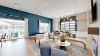 Located at 200 Villas Dr in Lavon, TX, this single-floor community amenity space is thoughtfully designed to serve as a vibrant social hub. The open-concept layout accommodates multiple activity zones, each with its own distinct character while flowing seamlessly into one another.

A bold teal accent wall anchors the recreation area, which features a ping-pong table and direct access to an outdoor area through sliding glass doors — filling the space with natural light and views of the surrounding community. Light wood-look flooring runs throughout, contributing to a warm, contemporary aesthetic.

The lounge zone offers comfortable seating arrangements with stylish accent chairs, upholstered poufs, and a round marble-top coffee table, all set atop a layered area rug beneath recessed lighting.

The wet bar is a standout feature, lined with crisp white cabinetry, quartz countertops, stainless steel appliances, and a large black-framed glass garage-style window that opens to the outdoors. A living moss wall display with neon signage adds a playful, modern touch to this entertaining area.

A café-style nook with a tufted banquette, round bistro tables, and a curated gallery wall rounds out the space, providing an intimate setting for conversation. Together, these zones create a well-appointed, multi-functional community gathering space.