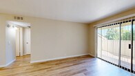 Located at 1241 Arnold Dr in Martinez, CA, this single-floor, one-bedroom unit offers a thoughtfully arranged layout that maximizes its intimate footprint. The combined kitchen and living area forms the heart of the space, featuring light wood-tone flooring throughout that lends a clean, cohesive aesthetic. The kitchen is equipped with white cabinetry, granite-style countertops, a built-in range, refrigerator, and a sink with ample counter space on both sides. A ceiling fan overhead in the living area provides both comfort and airflow. The living room is bathed in natural light through a large sliding glass door fitted with vertical blinds, which opens to an outdoor area with views of surrounding greenery — a standout feature that enhances the open, airy feel of the space. The bedroom is a comfortable size, finished with plush carpeting, warm neutral walls, and a window that allows natural light to filter in. A dedicated closet provides practical storage. Throughout the unit, warm beige tones on the walls, white trim, and consistent flooring choices create a calm, neutral palette. The overall ambiance is clean, functional, and well-lit, making this an efficient and welcoming living space.