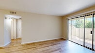 Located at 1241 Arnold Dr in Martinez, CA, this single-floor, one-bedroom unit offers a thoughtfully arranged layout that maximizes its intimate footprint. The combined kitchen and living area forms the heart of the space, featuring light wood-tone flooring throughout that lends a clean, cohesive aesthetic. The kitchen is equipped with white cabinetry, granite-style countertops, a built-in range, refrigerator, and a sink with ample counter space on both sides. A ceiling fan overhead in the living area provides both comfort and airflow. The living room is bathed in natural light through a large sliding glass door fitted with vertical blinds, which opens to an outdoor area with views of surrounding greenery — a standout feature that enhances the open, airy feel of the space. The bedroom is a comfortable size, finished with plush carpeting, warm neutral walls, and a window that allows natural light to filter in. A dedicated closet provides practical storage. Throughout the unit, warm beige tones on the walls, white trim, and consistent flooring choices create a calm, neutral palette. The overall ambiance is clean, functional, and well-lit, making this an efficient and welcoming living space.