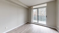 Located on the 10th floor at 151 Beecroft Road in North York, Toronto, this two-bedroom, one-bathroom unit offers a compact yet efficiently organized layout. Throughout the unit, light wood-tone laminate flooring and neutral warm-grey walls create a clean, consistent aesthetic that runs from room to room.

The spacious primary bedroom is the standout space, featuring large sliding glass doors that open onto a private balcony with open city views of the surrounding Toronto skyline. Natural light fills the room, enhancing its generous proportions. The second bedroom is well-sized with a large window admitting natural light and ample closet storage.

The kitchen features tile flooring, white cabinetry, granite-pattern laminate countertops, and a white electric range with overhead ventilation. The four-piece bathroom includes a full soaker tub with white subway tile surround, a toilet, and a granite-pattern countertop vanity. Hallway areas connect the rooms efficiently, with interior doors featuring classic six-panel detailing. Overall, the unit presents a straightforward, functional design suited to urban living in the North York area.