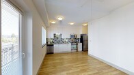 This single-floor space features a clean, contemporary design with an open layout that connects the kitchen and living areas seamlessly. The kitchen is a standout element, equipped with stainless steel appliances including a refrigerator, range with oven, and built-in microwave. Crisp white cabinetry extends from counter height to the ceiling, maximizing storage while contributing to a bright, airy atmosphere. A textured mosaic tile backsplash in muted grey and green tones adds visual interest and contrast against the white surfaces. The countertops provide ample workspace, and a stainless steel sink is positioned beneath a window that allows natural light to filter in. Flush-mount ceiling fixtures provide consistent overhead lighting throughout. Light-toned hardwood flooring runs continuously across the space, enhancing the sense of openness and warmth. The walls are finished in white, keeping the aesthetic minimal and versatile. The overall ambiance is modern and functional, with a neutral palette that offers flexibility for a variety of interior styles.