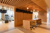 This modern fitness facility occupies a single floor within a high-rise building, offering a comprehensive workout environment defined by thoughtful design and an abundance of natural light. Floor-to-ceiling windows frame striking panoramic city skyline views throughout the cardio and cycling areas, creating an energizing atmosphere for training.

The facility is organized into distinct functional zones. A spacious strength training area features a full dumbbell rack, adjustable benches, cable machines, and plate-loaded equipment, all set against large mirrored walls that enhance the sense of openness. Light hardwood flooring runs throughout, lending a clean and welcoming aesthetic.

The cardio zone is lined with treadmills and stair climbers, each positioned to take full advantage of the city views beyond the expansive windows. Adjacent to this, a dedicated cycling area houses a row of stationary bikes and elliptical trainers, also bathed in natural light.

A distinctive lounge or common area features a warm wood-slatted ceiling, pendant globe lighting, a live green wall installation, and a natural wood communal table — offering a refined social space within the facility. Nearby, a service counter with cabinetry and a mini-fridge provides convenient amenities. An additional room with tatami-style flooring and an exposed concrete accent wall suggests space for stretching, yoga, or meditation, rounding out this well-appointed fitness center.