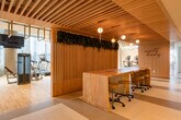 This modern fitness facility occupies a single floor within a high-rise building, offering a comprehensive workout environment defined by thoughtful design and an abundance of natural light. Floor-to-ceiling windows frame striking panoramic city skyline views throughout the cardio and cycling areas, creating an energizing atmosphere for training.

The facility is organized into distinct functional zones. A spacious strength training area features a full dumbbell rack, adjustable benches, cable machines, and plate-loaded equipment, all set against large mirrored walls that enhance the sense of openness. Light hardwood flooring runs throughout, lending a clean and welcoming aesthetic.

The cardio zone is lined with treadmills and stair climbers, each positioned to take full advantage of the city views beyond the expansive windows. Adjacent to this, a dedicated cycling area houses a row of stationary bikes and elliptical trainers, also bathed in natural light.

A distinctive lounge or common area features a warm wood-slatted ceiling, pendant globe lighting, a live green wall installation, and a natural wood communal table — offering a refined social space within the facility. Nearby, a service counter with cabinetry and a mini-fridge provides convenient amenities. An additional room with tatami-style flooring and an exposed concrete accent wall suggests space for stretching, yoga, or meditation, rounding out this well-appointed fitness center.