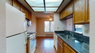 Located at 1782 D St in Hayward, California, this single-floor residence offers a well-organized layout with comfortable living spaces throughout. The kitchen is a standout feature, designed in a galley style with warm oak cabinetry, dark granite countertops, and hardwood flooring. It is equipped with a white electric range, refrigerator, built-in microwave, and dishwasher. A large skylight panel overhead floods the kitchen with natural light, while a window at the end of the galley provides views of the surrounding greenery. A ceiling fan adds to the comfort of the space. The open living area is generously sized, featuring plush carpeting, a fireplace, and sliding glass door access to the exterior. A pass-through connects the kitchen to the living space, enhancing the open feel. The bedroom offers carpeted flooring, a sliding-door closet with built-in shelving, and direct access to the bathroom. The bathroom is appointed with a granite-topped oak vanity, mirrored medicine cabinets, and a tub-shower combination with a frosted sliding glass enclosure and hardwood-style flooring. Throughout the home, neutral tones and consistent warm wood finishes create a cohesive and inviting ambiance.