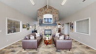 Located at 7918 S Serenera Way in West Jordan, Utah, this single-floor community space offers a welcoming and functional layout designed for gathering and relaxation. The open-concept living area immediately impresses with soaring vaulted ceilings that amplify the sense of space. A dramatic floor-to-ceiling stone fireplace serves as the room's focal point, complemented by patterned carpeting and comfortable seating. An abundance of natural light pours in through large, floor-to-ceiling windows along one wall, offering pleasant views of the surrounding neighborhood and greenery. The entry area features light tile flooring and seamlessly connects to the living space.

The kitchen is generously sized and thoughtfully designed, featuring warm honey-toned wood cabinetry extending to the ceiling for ample storage. Stainless steel appliances, including a range, microwave, and dishwasher, provide full functionality. A central island with seating for multiple guests makes the kitchen an ideal spot for casual dining or social interaction. Light tile flooring runs throughout the kitchen, and a double basin sink with a modern faucet adds a practical touch. Multiple windows in the kitchen allow for excellent natural light, creating a bright and inviting atmosphere throughout the entire space.