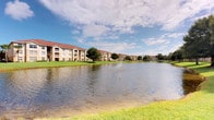 This residence is part of a Florida-style multi-building community distinguished by its warm stucco exteriors, red tile rooflines, and arched architectural accents. The community is positioned along a serene pond, offering picturesque waterfront views from the well-maintained grounds. Expansive stretches of manicured lawn frame the water's edge, while tall palm trees and mature tropical landscaping add to the inviting, resort-like atmosphere. Multiple three-story buildings are arranged thoughtfully around the pond, each featuring private balconies that overlook the water and greenery, creating a tranquil outdoor setting. The overall exterior ambiance reflects classic Floridian residential design, emphasizing open space, natural scenery, and a relaxed lifestyle. The community's grounds are notably well-kept, with vibrant shrubbery, ornamental plantings, and neatly trimmed grass contributing to its appealing curb appeal. The pond itself serves as a central landscape feature, enhancing the sense of calm and providing a natural focal point visible from multiple vantage points throughout the property. Interior images were not available for review.