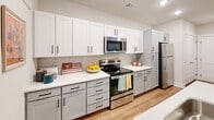 This well-designed 2-bedroom, 2-bathroom unit in Austin, TX (78705) offers a functional and modern single-floor layout. The open-concept living and kitchen area serves as the heart of the space, where light wood-style flooring flows throughout. The kitchen is equipped with stainless steel appliances — including a refrigerator, range, and over-the-range microwave — complemented by white shaker cabinetry, light quartz countertops, a neutral tile backsplash, and a peninsula with seating. Pendant lighting adds a stylish touch above the peninsula. The living area connects seamlessly to a private balcony through a sliding glass door, bringing in natural light and outdoor access. Both bedrooms are comfortably sized, each featuring ceiling fans, windows with blinds, and light wood flooring. One bedroom includes a double-door closet, ideal for storage. The two bathrooms are clean and modern: one features a tiled shower-tub combination, while the other offers a single vanity with white cabinetry and a large mirror. Recessed lighting throughout the unit ensures a bright, welcoming ambiance. The overall aesthetic is contemporary and cohesive, making this Austin unit a comfortable and practical living space.
