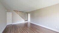 This two-story home offers three bedrooms and two bathrooms across a thoughtfully laid-out floor plan. The main level serves as the larger of the two floors and features a living room with wood-look flooring, neutral gray walls, and a staircase with a white-railed banister leading to the upper level. The kitchen is a standout space, equipped with two-tone cabinetry—glossy white upper cabinets contrasting with wood-grain lower cabinets—white countertops, a tiled backsplash in a muted teal, and stainless steel appliances including a refrigerator and dishwasher. One of the bathrooms is located on the main level and includes a vanity with a white countertop and tiled flooring, with a stacked washer and dryer conveniently integrated nearby. The second bathroom features a pedestal-style vanity with a medicine cabinet above. The upper floor houses the bedrooms, each finished with plush carpet and neutral-toned walls. The primary bedroom is generously sized and includes direct access to a closet and bathroom. Additional bedrooms feature built-in closets with bifold doors and windows that bring in natural light. One bedroom on the main level features wood-look flooring and a louvered closet door. Throughout the home, clean white trim and a consistent neutral palette create a cohesive, modern ambiance.