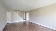 This two-story home offers three bedrooms and two bathrooms across a thoughtfully laid-out floor plan. The main level serves as the larger of the two floors and features a living room with wood-look flooring, neutral gray walls, and a staircase with a white-railed banister leading to the upper level. The kitchen is a standout space, equipped with two-tone cabinetry—glossy white upper cabinets contrasting with wood-grain lower cabinets—white countertops, a tiled backsplash in a muted teal, and stainless steel appliances including a refrigerator and dishwasher. One of the bathrooms is located on the main level and includes a vanity with a white countertop and tiled flooring, with a stacked washer and dryer conveniently integrated nearby. The second bathroom features a pedestal-style vanity with a medicine cabinet above. The upper floor houses the bedrooms, each finished with plush carpet and neutral-toned walls. The primary bedroom is generously sized and includes direct access to a closet and bathroom. Additional bedrooms feature built-in closets with bifold doors and windows that bring in natural light. One bedroom on the main level features wood-look flooring and a louvered closet door. Throughout the home, clean white trim and a consistent neutral palette create a cohesive, modern ambiance.