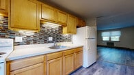 Located at 17 Regan St in Vernon Rockville, Connecticut, this single-floor unit offers a practical and comfortable layout designed for everyday living. The space is unified throughout by durable wood-look flooring in cool grey and warm toned finishes, lending a clean, contemporary feel to each room.

The kitchen is a functional highlight, featuring an ample run of warm honey-toned cabinetry — both upper and lower — paired with white countertops and a stainless steel sink. A decorative mosaic tile backsplash in earth tones adds a touch of character, while a white refrigerator and electric range complete the space. The kitchen opens toward the living area, allowing for an easy flow between spaces.

The living area is generously sized, with natural light filtering in through a window fitted with blinds and a baseboard heating unit positioned along the wall. A built-in open shelving unit provides convenient storage and acts as a subtle room divider. The bedroom areas are well-proportioned, each featuring the same wood-look flooring, neutral walls, and windows that bring in natural light. At least one bedroom includes a closet with built-in shelving and hanging rod.

The bathroom features a full soaking tub with a tub surround, classic pink tile walls, and a window that provides natural ventilation. Baseboard heating is present throughout the unit, ensuring year-round comfort.