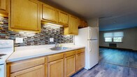 Located at 17 Regan St in Vernon Rockville, Connecticut, this single-floor unit offers a practical and comfortable layout designed for everyday living. The space is unified throughout by durable wood-look flooring in cool grey and warm toned finishes, lending a clean, contemporary feel to each room.

The kitchen is a functional highlight, featuring an ample run of warm honey-toned cabinetry — both upper and lower — paired with white countertops and a stainless steel sink. A decorative mosaic tile backsplash in earth tones adds a touch of character, while a white refrigerator and electric range complete the space. The kitchen opens toward the living area, allowing for an easy flow between spaces.

The living area is generously sized, with natural light filtering in through a window fitted with blinds and a baseboard heating unit positioned along the wall. A built-in open shelving unit provides convenient storage and acts as a subtle room divider. The bedroom areas are well-proportioned, each featuring the same wood-look flooring, neutral walls, and windows that bring in natural light. At least one bedroom includes a closet with built-in shelving and hanging rod.

The bathroom features a full soaking tub with a tub surround, classic pink tile walls, and a window that provides natural ventilation. Baseboard heating is present throughout the unit, ensuring year-round comfort.