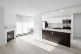 Located on Battleford Road in Mississauga, Ontario, this well-appointed single-floor unit showcases a clean, modern aesthetic throughout, characterized by crisp white walls, recessed lighting, and an abundance of natural light.

The kitchen is a standout feature, offering a galley-style layout with tall white cabinetry, stainless steel appliances including a refrigerator, stove, built-in microwave, and dishwasher, complemented by a light-toned countertop and large-format white tile flooring. A dark-finished kitchen island with a generous quartz-style countertop provides additional prep and seating space, seamlessly connecting the kitchen to the living area.

The living area is bright and open, anchored by a white-mantled fireplace with a classic brick surround. Large floor-to-ceiling windows dressed with vertical blinds flood the space with natural light and provide views of the surrounding neighbourhood. Light wood-look flooring flows throughout the living and sleeping areas, creating a warm yet contemporary feel.

The bedroom is spacious and sun-drenched, featuring a large sliding-door closet with built-in shelving and hanging space, offering practical storage solutions. A wide window with vertical blinds and a baseboard heating unit lines one wall, ensuring comfort year-round.

Overall, this unit presents a cohesive, modern design with thoughtful finishes and bright, livable spaces.