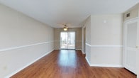 Located at 6000 Mabeline Rd in Hanahan, South Carolina, this two-story home offers a practical and comfortable layout with consistent finishes throughout. The main living area is bright and open, showcasing warm hardwood flooring, neutral-toned walls with white chair rail molding, and a ceiling fan overhead. A sliding glass door floods the space with natural light and provides a view of the outdoors, creating an inviting atmosphere. A second living or flex space mirrors this aesthetic, featuring the same hardwood floors, chair rail detail, and a vaulted ceiling that adds a sense of height and openness, along with two windows that bring in additional natural light. The kitchen is well-equipped with rich wood cabinetry, laminate countertops, and a full suite of white appliances including an electric range, over-the-range microwave, dishwasher, and refrigerator. Ample upper and lower cabinet storage provides generous workspace for everyday cooking needs. A dedicated laundry nook houses a front-loading washer and dryer set alongside overhead wire shelving for additional storage. The home's consistent hardwood flooring, textured ceilings, and clean white trim create a cohesive and functional living environment throughout both levels.