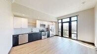 Located in Tulsa, Oklahoma, this modern studio unit offers a well-designed single-floor layout that efficiently maximizes its compact footprint. The open-plan living and kitchen area is immediately welcoming, anchored by light wood luxury vinyl flooring that runs throughout the space and contributes to a clean, contemporary aesthetic.

The kitchen is a standout feature, showcasing a two-tone design with navy lower cabinetry and crisp white upper cabinets paired with open shelving. A white subway tile backsplash, granite-look countertops, and a full suite of stainless steel appliances — including a refrigerator with ice maker, electric range, microwave, and dishwasher — complete the culinary space. A wall-mounted mini-split HVAC unit ensures year-round comfort.

Floor-to-ceiling black-framed windows and a glass balcony door flood the living area with abundant natural light while offering views of the surrounding Tulsa cityscape. The bedroom area benefits from the same expansive windows and access to the balcony.

A dedicated hallway leads to the bathroom, which features a walk-in shower with white subway tile surround and chrome fixtures. An adjacent room provides generous built-in shelving and clothing rods, offering well-organized storage. Recessed lighting and a neutral color palette tie the entire space together with a polished, modern feel.