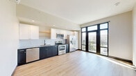 Located in Tulsa, Oklahoma, this modern studio unit offers a well-designed single-floor layout that efficiently maximizes its compact footprint. The open-plan living and kitchen area is immediately welcoming, anchored by light wood luxury vinyl flooring that runs throughout the space and contributes to a clean, contemporary aesthetic.

The kitchen is a standout feature, showcasing a two-tone design with navy lower cabinetry and crisp white upper cabinets paired with open shelving. A white subway tile backsplash, granite-look countertops, and a full suite of stainless steel appliances — including a refrigerator with ice maker, electric range, microwave, and dishwasher — complete the culinary space. A wall-mounted mini-split HVAC unit ensures year-round comfort.

Floor-to-ceiling black-framed windows and a glass balcony door flood the living area with abundant natural light while offering views of the surrounding Tulsa cityscape. The bedroom area benefits from the same expansive windows and access to the balcony.

A dedicated hallway leads to the bathroom, which features a walk-in shower with white subway tile surround and chrome fixtures. An adjacent room provides generous built-in shelving and clothing rods, offering well-organized storage. Recessed lighting and a neutral color palette tie the entire space together with a polished, modern feel.