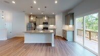 Located at 507 Merrion Park Lane in Morrisville, NC, this three-floor home offers a thoughtfully designed layout with contemporary finishes throughout. The kitchen serves as a central highlight, featuring a large island with speckled granite countertops, an integrated sink, and decorative glass pendant lighting overhead. Gray shaker-style cabinetry pairs with a white subway tile backsplash, and stainless steel appliances complete the space. Hardwood-style flooring extends through the main living areas, adding warmth and continuity.

The living area opens to the outdoors via glass French doors flanked by multiple windows, filling the space with natural light and providing access to the exterior. A ceiling fan enhances comfort in this bright, open room.

The primary bathroom is finished with wood-look tile flooring, a dual-sink white vanity, a glass-enclosed walk-in shower, and a private water closet. A secondary bathroom offers a clean, minimalist design with a tub-shower combination and neutral tile flooring.

Bedrooms are carpeted for comfort, with windows offering neighborhood views. A dedicated laundry area houses full-sized side-by-side washer and dryer units with overhead wire shelving for added storage. The home's clean, neutral palette creates a bright and welcoming atmosphere throughout all three floors.