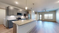 Located at Heritage Towne Blvd in Midlothian, TX, this well-appointed one-bedroom, one-bathroom unit offers a thoughtfully designed open-concept layout with modern finishes throughout. The kitchen and living area flow seamlessly together, anchored by a large center island with a white quartz countertop, undermount sink, and stylish pendant lighting. Gray shaker-style cabinetry, a classic tile backsplash, and a full suite of stainless steel appliances — including a french door refrigerator, microwave, and range — complete the kitchen. Light wood-look flooring runs throughout the main living areas, enhancing the bright and airy atmosphere. The living room features a ceiling fan and direct access to a private balcony, offering outdoor views of the surrounding neighborhood. The bedroom is generously sized with tall ceilings, plush carpet flooring, and multiple windows that bring in abundant natural light. A dedicated closet with built-in shelving and hanging rods provides ample storage. The bathroom includes a soaking tub with a tiled surround, open shelving, and direct access to the walk-in closet. Additional practical features include a utility room and in-unit laundry facilities, rounding out this functional and stylish home.