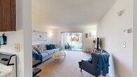 This efficiently designed 1-bedroom, 1-bathroom single-floor residence offers a thoughtful layout across four distinct rooms. The living room serves as the heart of the space, featuring soft carpeted flooring, bright white walls, and a large sliding glass door that floods the area with natural light while providing direct access to a private outdoor patio and green garden area. The open, airy atmosphere is enhanced by clean lines and a neutral color palette.

The kitchen is laid out in a galley-style configuration, featuring dark wood cabinetry, white countertops, hardwood-style flooring, and standard appliances including an electric range, dishwasher, and refrigerator — offering efficient use of space for everyday cooking.

The bedroom is a comfortably sized retreat with plush carpeting, a window with vertical blinds for light control, and clean white walls that create a calm, restful atmosphere.

The bathroom is finished with tile flooring, a shower/tub combination, a single vanity with mirror cabinet, and straightforward, functional fixtures throughout.

Overall, this residence presents a practical and livable layout with a welcoming ambiance, highlighted by its natural light and direct outdoor access from the living area.