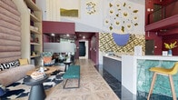Located at 661 Wedgewood Ave in Nashville's 37203 corridor, this single-floor communal space is a bold, design-forward interior that blends art, function, and personality. The entrance greets visitors with soaring double-height ceilings, floor-to-ceiling glass doors, and geometric patterned tile flooring that transitions seamlessly throughout the space. A welcoming reception desk anchors the lobby area, flanked by a striking mural of oversized floral artwork that spans the upper wall.

A lounge seating area features eclectic furnishings — including a tufted teal bench, patterned armchairs, a cowhide rug, and open built-in shelving styled with books and curated décor. Adjacent to the lobby, a prominent bar counter clad in richly veined green marble stone hosts a row of gold bar stools, serving as a central social hub.

The space extends into a dedicated dining and meeting area, defined by deep plum-toned walls and ceilings, a long communal table surrounded by colorful mismatched chairs, and pendant lighting overhead. Large floor-to-ceiling windows flood this area with natural light and offer open views of the surrounding greenery. A mezzanine level with metal railings overlooks the main floor, adding vertical dimension and architectural depth to the overall space.
