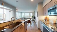 This thoughtfully designed single-floor residence offers a seamless blend of modern aesthetics and functional living. The open-concept layout connects the kitchen, dining, and living areas into one cohesive, light-filled space. Large windows throughout flood the interior with natural light and provide views of the surrounding neighborhood, enhancing the airy, welcoming atmosphere.

The kitchen is a standout feature, equipped with stainless steel appliances including a gas range, microwave, and refrigerator. Warm wood-tone cabinetry pairs with dark countertops and a deep farmhouse-style sink set into a central island, while a glass subway tile backsplash adds a refined touch. Pendant lighting above the island adds both style and function.

The living and dining areas are generously proportioned, with warm wood-look flooring that runs throughout the main living spaces. A wall of oversized windows anchors the living room, creating a bright and comfortable retreat.

The bedroom is a calm, well-sized sanctuary featuring large windows, soft neutral tones, and a sliding-door closet with built-in shelving. The bathroom is finished with clean white subway tile surrounding the tub and shower combination, complemented by chrome hardware for a crisp, modern look. Overall, the residence exudes a contemporary yet comfortable character.