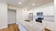 This well-appointed 2-bedroom, 2-bathroom unit is laid out across a single floor, offering a thoughtfully designed open-concept floor plan. The kitchen serves as a central highlight, featuring a large granite-topped island with an integrated sink, crisp white shaker cabinetry extending to the ceiling, and a full suite of stainless steel appliances including a refrigerator, electric range, and over-the-range microwave. Warm hardwood-style flooring flows consistently throughout the entire unit, creating a cohesive and inviting aesthetic.

The living and kitchen areas are bright and open, illuminated by recessed lighting that enhances the clean, neutral color palette. Both bedrooms are generously proportioned, each benefiting from multiple windows dressed with white horizontal blinds that allow for ample natural light. The primary bedroom connects to a walk-in closet equipped with built-in shelving and hanging rods for organized storage, as well as direct access to a private en-suite bathroom.

Both bathrooms are finished with granite-topped white vanities, overhead cabinetry for additional storage, and stylish brushed nickel fixtures. The second bathroom is equally well-appointed, maintaining the same refined design language found throughout. A dedicated entrance and additional closet space round out this functional and modern unit.