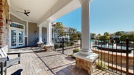 Located at 285 Park Ave in Pooler, Georgia, this single-level covered outdoor patio area offers a refined and inviting community amenity space. The patio is defined by striking white columnar pillars set on natural stone bases, lending a classic Southern architectural character to the space. The flooring consists of attractive interlocking brick pavers that extend throughout the covered and open areas, adding texture and visual warmth underfoot.

The space is furnished with modern outdoor seating, including a sofa and chairs upholstered in bold blue cushions paired with a sleek coffee table, creating a comfortable and stylish lounge area ideal for relaxation and social gatherings. The covered portion of the patio provides ample shade while remaining open on the sides, allowing for natural light and fresh air to flow freely through the space.

A wrought iron fence borders the patio, offering a clear view of the community pool area and lush surrounding landscaping, including mature trees and palms that contribute to the vibrant outdoor atmosphere. The natural stone accent walls along the building's exterior add an additional layer of architectural detail and durability. Under the abundant Georgia sunshine, this outdoor space presents a welcoming, resort-like ambiance suited for both casual and communal use.