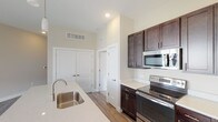 This well-appointed single-floor residence offers a thoughtfully designed layout with modern finishes throughout. The open-concept kitchen serves as the heart of the home, showcasing rich dark espresso cabinetry with sleek brushed nickel hardware, light quartz countertops, and a full suite of stainless steel appliances including an electric range, built-in microwave, and French door refrigerator. A generously sized center island with an undermount sink and elegant pendant lighting above makes the kitchen both functional and visually striking. Wood-style flooring runs throughout the main living and kitchen areas, adding warmth and continuity.

The living area features durable hardwood-style flooring, a sliding glass door with vertical blinds, and multiple windows that fill the space with natural light and outdoor views. The bedrooms are carpeted for comfort, each equipped with a ceiling fan and windows overlooking the surrounding greenery. The bathrooms are finished with dark vanity cabinetry, quartz countertops, wood-style flooring, and a tub-shower combination in the full bath, along with a dedicated over-toilet storage cabinet in the secondary bathroom. A separate in-unit laundry room with full-size washer and dryer completes this practical and stylish residence.