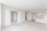 This single-floor residence offers a clean, functional layout with a warm, neutral color palette throughout. The expansive living area is finished with plush wall-to-wall carpeting and features a textured ceiling, with natural light entering through a window alongside a built-in radiator unit. A pass-through counter connects the living space directly to the kitchen, which is outfitted with white cabinetry, light granite-style countertops, tile flooring, a full appliance suite including an electric range and dishwasher, and a window above the sink. A dedicated laundry closet adjacent to the kitchen houses a stacked washer and dryer for added convenience. The bedrooms are generously proportioned, each featuring soft carpeting and neutral walls, with select rooms offering closet access via classic six-panel doors. The primary full bathroom includes a tiled tub-shower combination, mosaic tile flooring, a vanity with a white countertop, and a mirror. A second half-bath provides a toilet and vanity, also with mosaic tile flooring. Double bi-fold doors off the living area open to additional closet or storage space, enhancing the overall practicality of this well-organized residence.