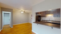 This single-floor residence at 707 N 25th St in Reading, PA offers a practical and well-maintained layout highlighted by warm hardwood flooring that extends throughout the living, dining, and bedroom areas. The open-concept living and dining space is generously sized, featuring neutral gray walls, clean white baseboards, and a ceiling fan with integrated lighting that adds both function and comfort. A pass-through peninsula connects this area to the kitchen, which is equipped with rich dark wood cabinetry, a white subway tile backsplash, granite-style countertops, and black appliances including a full-size refrigerator, range, and microwave. Under-cabinet lighting adds practicality to the kitchen's efficient galley-style layout. The bedroom offers a comfortable footprint with a wall-mounted air conditioning unit and a window that allows natural light and outdoor views. The bathroom features white tile wainscoting, tile flooring, and a full tub and shower combination with chrome fixtures and a grab bar. A hallway connects the rooms, contributing to a straightforward and functional floor plan throughout the space.