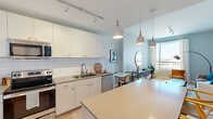 This 1-bedroom, 1-bathroom unit in New Orleans, LA offers a thoughtfully designed open-concept layout that maximizes every square foot. The kitchen is a standout feature, boasting white flat-front cabinetry with gold hardware, white subway tile backsplash, stainless steel appliances, and a central island with quartz countertops illuminated by pendant lighting. The kitchen flows seamlessly into a dining nook and a bright living area, where a large window frames sweeping city views and fills the space with natural light. Light-toned hardwood floors run throughout the main living areas, enhancing the airy, contemporary feel. The bedroom is a serene retreat, featuring a generous window with city views, a ceiling fan, and easy access to ample closet storage with built-in shelving. The bathroom is elegantly appointed with a teal-blue vanity, white quartz countertop, a large mirror with gold-toned pendant lighting, and decorative tile flooring, while a separate shower/tub combination and walk-in closet provide added functionality. Soft, neutral tones with cool blue accents are carried throughout the unit, creating a cohesive and calming aesthetic that reflects modern urban living in the heart of New Orleans.