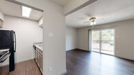This 1-bedroom, 1-bathroom residence offers a practical and comfortable single-floor layout designed for efficient living. Dark hardwood-style flooring runs consistently throughout the main living areas and bedroom, lending a warm, cohesive aesthetic to the space. The open living and dining area is bright and airy, anchored by a ceiling fan with integrated lighting and a sliding glass door that opens onto a private balcony, filling the room with natural light and offering views of surrounding greenery. The galley-style kitchen is positioned adjacent to the main living area and features granite countertops, dark cabinetry, and black appliances including a range and refrigerator, along with a skylight that provides additional overhead illumination. The bedroom is a comfortable size, equipped with its own ceiling fan, a window with blinds for natural light and privacy, and access to two closets for ample storage. The bathroom is clean and functional, featuring a full tub-shower combination with large white tile surround, granite vanity countertop, and dark cabinetry. Textured walls and ceilings add architectural character throughout, while consistent neutral tones create a calm, move-in-ready environment.