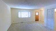 This two-floor home offers a straightforward and functional layout designed for comfortable everyday living. The main level features an open living area with plush wall-to-wall carpeting that adds warmth underfoot. A large window with decorative diamond-patterned leaded glass panes serves as a focal point, allowing natural light to fill the room and create a bright, airy atmosphere. A classic wood-panel entry door, also fitted with a leaded glass inset window, provides a welcoming entry point while continuing the home's charming character. Flush-mounted ceiling lighting and floor-level heating vents speak to the home's practical and efficient design. The neutral, light-toned walls offer a clean and versatile backdrop throughout. The second floor extends the living space further, providing additional room configurations suited to a variety of needs. Overall, the home presents a clean, well-maintained environment with consistent finishes across its two levels, making it a solid and adaptable space ready for personal customization.