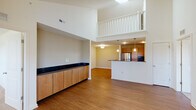 This two-story residence is defined by its dramatic double-height ceilings in the main living area, creating an expansive, airy atmosphere that immediately draws the eye upward to a white-railed second-floor loft overlooking the space below. The main level features warm hardwood-style flooring throughout, anchored by a generously sized open living area with vaulted ceilings and a built-in storage unit with wood cabinetry topped by a dark countertop — a practical and stylish architectural detail. An arched doorway adds a refined touch, connecting the living space to adjoining rooms.

The kitchen is efficiently designed with stainless steel appliances, including a refrigerator, electric range, and microwave. Dark lower cabinetry contrasts with lighter upper cabinets, while pendant lighting adds warmth over the bar-height counter that separates the kitchen from the living area. Two full bathrooms are present, each with hardwood-style flooring, a soaking tub, and wood vanity cabinetry with light countertops.

Upstairs, the loft-style second floor is carpeted and bright, offering a flexible open layout with vaulted ceilings. Additional carpeted bedrooms provide natural light through multiple windows and ceiling fans, contributing to a comfortable and well-lit environment throughout.
