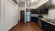 Located at 102 W Superior St in the heart of downtown Fort Wayne, Indiana, this single-floor loft-style unit blends industrial character with modern finishes throughout. Rich, dark hardwood flooring runs continuously across the space, anchoring each room with warmth and cohesion.

The kitchen is a standout feature, outfitted with dark espresso cabinetry extending to the ceiling, granite countertops, and a full suite of stainless steel appliances including a refrigerator, range, microwave, and dishwasher. Exposed ductwork and industrial-style pendant lighting add an authentic urban loft aesthetic to the cooking and living areas.

The living area is generously proportioned with soaring ceilings that enhance the open, airy feel. A secondary kitchenette or wet bar area with matching dark cabinetry and a sink provides added functionality.

The bedroom offers a quiet retreat with tall ceilings and windows overlooking the surrounding downtown cityscape, filling the room with natural light. A second windowed room provides additional flexible living or office space with similar city views.

The bathroom is well-appointed with a dark vanity topped with granite, a large mirror, built-in shelving for storage, and a full tub-shower combination. The overall design of the space strikes a balance between industrial urban loft character and comfortable, contemporary living in the heart of Fort Wayne.
