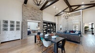This single-story amenity space is defined by its striking architectural design, most notably in the grand common area where soaring ceilings are accented by dark, exposed wood beams and dramatic stone accent walls that frame arched passageways. Rich hardwood flooring flows throughout, complemented by a mix of eclectic, modern furnishings and statement chandeliers that lend warmth and character. Built-in shelving units with navy cabinetry add both function and visual depth to the space.

The lounge area features comfortable seating arrangements alongside a built-in work ledge, offering versatile space for relaxation or casual productivity. A dedicated business center provides desktop workstations and soft seating beneath tall windows that flood the room with natural light. A private conference room equipped with a wall-mounted display and a pendant light serves small group meetings effectively.

The game lounge includes a billiards table, a mounted television, and casual seating amid designer carpet, with glass-paneled doors opening to adjacent areas. The fitness studio is generously sized, with light wood flooring, full-length mirrors, ballet barres, spinning bikes, a projection screen, and a comprehensive selection of exercise equipment, all beneath a tray ceiling with overhead fans.