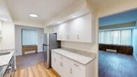 Located at 1199 Whitney Ave in Hamden, Connecticut, this 2-bedroom, 1-bathroom residence offers a well-organized single-floor layout with a clean, neutral aesthetic throughout. Rich hardwood-style flooring flows seamlessly across the living areas and bedrooms, creating a warm and cohesive feel.

The open living room is generously proportioned, bathed in natural light from vertical-blind-covered windows, and features a classic baseboard heating unit. It connects directly to the kitchen, which stands out as a highlight of the unit. The kitchen is outfitted with white shaker-style cabinetry, gleaming granite countertops, stainless steel appliances including a refrigerator and range, a deep single-basin sink, and recessed lighting overhead — a modern and functional space for cooking and entertaining.

Both bedrooms are comfortably sized, with the primary bedroom offering a closet with paneled bi-fold doors and access to the hallway. The second bedroom mirrors the same warm flooring and neutral wall tones found throughout.

The full bathroom is finished with light tile flooring, a single-sink vanity with cabinetry below, a wide mirror with built-in medicine cabinet, and a full tub and shower combination, providing a clean and practical space. The overall ambiance is bright, tidy, and move-in ready.