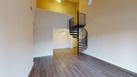 This two-story residence in Louisville, Kentucky offers a striking and functional layout defined by standout architectural details. The main living area immediately impresses with soaring double-height ceilings accentuated by a bold yellow accent wall and a dramatic black wrought-iron spiral staircase that serves as a central design feature. Hardwood-style flooring runs throughout the main level, complemented by ceiling fans that enhance comfort and airflow.

The kitchen is well-equipped with warm honey-toned cabinetry, light stone-finish countertops, and white appliances including a range, dishwasher, refrigerator, and microwave, all set above durable wood-look flooring. An additional room on the main level features hardwood-style floors and an open closet with built-in shelving.

Upstairs, the loft-style landing opens to a vaulted-ceiling space with a ceiling fan and sliding glass door leading to an outdoor balcony. Multiple carpeted bedrooms provide a soft, comfortable feel, with natural light flowing in through double-pane windows offering neighborhood views. A full bathroom on this level includes a vanity with rich wood cabinetry, a tub-shower combination, and wood-look flooring. The upper level also features an open loft area with vaulted ceilings, ideal as a flexible living or workspace.
