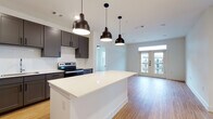 Located at 1516 Nash Hernandez Sr Rd in Austin's 78702 zip code, this single-floor residence offers a thoughtfully designed open-concept layout with clean, contemporary finishes throughout. The kitchen serves as the heart of the home, showcasing dark gray shaker-style cabinetry, white quartz countertops, a subway tile backsplash, and a full suite of stainless steel appliances including a refrigerator, electric range, and dishwasher. A central island with pendant lighting adds both function and style, flowing seamlessly into the living area. Warm bamboo-style hardwood flooring extends across the main living spaces, complementing the bright, neutral color palette. The living area is bathed in natural light and features a set of French doors with a transom window above, opening to an outdoor balcony with views of the surrounding neighborhood. The bedrooms are carpeted for comfort, each offering generous windows with views of either the urban streetscape or lush treetops. The bathrooms feature dark cabinetry with quartz countertops and direct access to well-appointed walk-in closets with built-in shelving and hanging rods. Recessed lighting and modern pendant fixtures add a polished finishing touch throughout this well-appointed Austin residence.