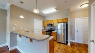 This single-floor residence offers a well-designed, functional layout that balances open living areas with defined private spaces. The kitchen serves as a central highlight, outfitted with warm honey-toned cabinetry, stainless steel appliances including a refrigerator, electric range, built-in microwave, and dishwasher. A tiled backsplash adds a clean, polished detail, while a peninsula breakfast bar with pendant lighting above creates a natural transition into the adjacent living and dining area. Rich hardwood-style flooring runs throughout the main living spaces, adding warmth and continuity. The living area is generously sized, featuring crown molding, a ceiling fan with integrated lighting, and windows that invite natural light. A door from this space provides direct exterior access, enhancing connectivity. The bedroom offers plush carpeting, a ceiling fan, and a window with natural light. The bathroom is well-appointed with a single-sink vanity with wood cabinetry, a full tub/shower combination, and hardwood-style flooring. Throughout the space, neutral taupe wall tones create a cohesive, understated palette that complements each room's features. The overall ambiance is practical and inviting, with thoughtful details that support comfortable everyday living.