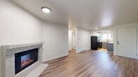 Located at 17520 Linden Ave N in Shoreline, WA, this two-bedroom, two-bathroom residence offers a thoughtfully designed layout with modern finishes throughout. The living room serves as the heart of the home, featuring warm wood-look luxury vinyl plank flooring, a corner brick-surround electric fireplace, and a sliding glass door that opens to a private balcony with lush outdoor views, filling the space with natural light.

The kitchen is well-appointed with a two-tone cabinet scheme — white upper cabinets paired with gray lower cabinets — complemented by light countertops, stainless steel appliances including a dishwasher, a black refrigerator, and a window above the sink that brings in additional natural light. Track lighting overhead enhances the functional workspace.

Both bedrooms are carpeted and offer a calm, neutral palette with windows that overlook the surrounding greenery. Baseboard heating units are present in each room for comfortable climate control.

The two bathrooms are finished in a clean, contemporary style with gray vanity cabinets, white countertops, framed mirrors, and light wood-look tile flooring. One bathroom features a full shower-tub combination with a curved curtain rod. The overall aesthetic is cohesive, modern, and move-in ready.