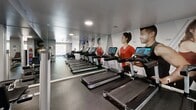 The Georgetown of Saint Louis Fitness Center at 7880 Chatwell Drive in St. Louis, MO, is a comprehensively equipped exercise facility spread across a single, generously sized floor. The space is divided into distinct functional zones, each designed to support a full range of workout routines.

The strength training area features a full rack of dumbbells with an adjustable bench, a multi-station cable machine, and additional free-weight equipment, all set against a large floor-to-ceiling mirror that enhances the sense of space and allows users to monitor their form. The Georgetown of Saint Louis branding is prominently displayed on the wall, adding a polished, community-centered identity to the space.

The cardio zone is outfitted with multiple treadmills and stationary cycling bikes, each equipped with individual digital screens for an interactive workout experience. Bold, large-format fitness-themed wall murals energize the room and contribute to a motivating atmosphere.

Throughout the facility, durable rubber flooring provides safety and comfort underfoot, while recessed and flush-mounted ceiling lights ensure consistent, well-distributed illumination. Natural light filters in through windows near the entrance, adding brightness to the environment. The neutral gray walls and clean white trim maintain a modern, professional aesthetic. Safety signage, emergency equipment, and facility notices are clearly posted throughout.
