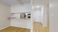 This single-floor residence offers a clean, modern aesthetic throughout, characterized by light-toned walls, warm light wood flooring in the main living areas, and a neutral color palette that creates a bright and welcoming ambiance.

The kitchen is a standout feature, outfitted with crisp white cabinetry, granite-look countertops, and a full suite of stainless steel appliances including a refrigerator, range, and microwave. A pass-through peninsula connects the kitchen to the open living area, enhancing the sense of openness and making the space ideal for everyday living. The living area is generously proportioned, with a ceiling fan overhead and direct sightlines to the kitchen and hallway beyond.

A separate room features large sliding glass doors that invite abundant natural light and offer views of the surrounding outdoor scenery, complemented by baseboard heating. The bedrooms are finished with soft wall-to-wall carpeting, windows with outdoor views, and ample closet space with sliding doors. 

The bathroom is well-appointed with white shaker-style cabinetry, granite countertops, an undermount sink, brushed gold hardware, and a tub-shower combination, offering a clean and updated feel. The overall layout is functional and cohesive, making efficient use of space across all rooms.