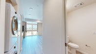 Located at 2701 Shattuck St in Berkeley, CA, this efficiently designed studio unit offers a well-planned single-floor layout that maximizes functionality within a compact footprint. Light-toned luxury vinyl plank flooring runs throughout the entire space, contributing to a clean, cohesive aesthetic.

The open living area is brightened by a large picture window that frames outdoor views of the surrounding Berkeley neighborhood, allowing abundant natural light to fill the room. A wall-mounted mini-split HVAC unit provides individual climate control. Recessed ceiling lighting adds to the bright, airy atmosphere.

The kitchenette is thoughtfully equipped with warm-toned wood cabinetry extending from floor to ceiling, offering generous storage. Stainless steel appliances — including a full-size refrigerator and built-in microwave — complement the smooth white countertops. An induction cooktop and a single-basin sink complete the functional kitchen setup.

The bathroom features a clean, accessible design with light tile-style flooring, a bathtub with grab bars, and a toilet. The neutral, cream-toned walls throughout the unit enhance the sense of openness. This unit is well-suited for those seeking a modern, low-maintenance living space in a convenient Berkeley location.