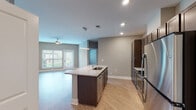 Located at 921 Trailwood Dr in Raleigh, NC, this single-floor residence offers a thoughtfully designed open-concept layout finished with light wood-style flooring throughout the main living areas and neutral gray tones on the walls. The kitchen serves as the centerpiece of the home, featuring a large island with a granite countertop and undermount sink, dark espresso cabinetry extending to the ceiling, stainless steel appliances including a refrigerator, range, and microwave, and a sleek linear pendant light overhead. The kitchen flows seamlessly into the living area, which benefits from abundant natural light through large windows and a door providing direct access to an outdoor balcony. A ceiling fan adds comfort to the living space. Carpeted bedrooms offer a softer feel, with one bedroom featuring a walk-in closet with built-in wire shelving. The bathroom is well-appointed with a granite-topped vanity, dark cabinetry, a large mirror, and a tub-shower combination. A dedicated in-unit laundry area with a washer and dryer is conveniently accessible from the kitchen corridor, adding practical functionality to this well-rounded residence.