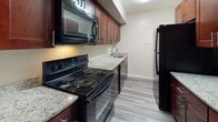 This single-floor residence is designed with a practical and open layout, highlighted throughout by dark hardwood-style flooring that lends a cohesive, modern feel. The spacious living and dining area serves as the heart of the unit, bathed in natural light from a large sliding glass door that opens directly to an outdoor patio, offering views of the surrounding neighborhood. A pendant light fixture adds a finishing touch to the dining space, while a wall-mounted heater ensures year-round comfort. A half-wall counter seamlessly connects the living area to the galley-style kitchen, which is outfitted with rich dark wood cabinetry, granite countertops, and black appliances including a range, over-range microwave, and refrigerator. The bedrooms are well-proportioned, each featuring hardwood-style flooring and windows that bring in natural light. One bedroom includes a ceiling fan, while another boasts two separate closets — one a walk-in — providing generous storage. The bathroom is clean and functional, featuring a full tub-shower combination with chrome fixtures. Additional storage is accessible throughout the unit, completing this well-appointed space.