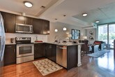 Located in the heart of Atlanta's prestigious Buckhead district (30326), this thoughtfully designed single-floor residence offers a polished urban living experience with contemporary finishes throughout. The open living area features warm hardwood flooring, a coffered ceiling detail, and an inviting arrangement centered around a substantial upholstered sofa set. The space is accented with eclectic artwork and ambient lighting that creates a sophisticated yet comfortable atmosphere. The kitchen is outfitted with sleek dark cabinetry, stainless steel appliances including a refrigerator, range, and built-in microwave, complemented by granite countertops and hardwood floors. A pendant light and undermount sink add refined finishing touches. The bedroom is a standout space, featuring a deep navy accent wall that creates a dramatic backdrop for the tufted upholstered headboard and layered bedding. Floor-to-ceiling windows flood the room with natural light while offering sweeping views of the surrounding Atlanta skyline, reinforcing the elevated urban setting. The bathroom is finished with tile flooring, dark espresso cabinetry, granite countertops, a large vanity mirror, and a glass-enclosed walk-in shower. Together, these spaces combine to deliver a modern, design-forward residence well-suited for city living in one of Atlanta's most sought-after neighborhoods.